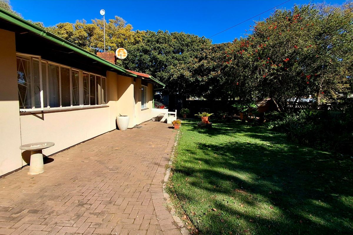 A rear exterior view featuring a paved patio area adjacent to a well-maintained lawn and mature garden trees.