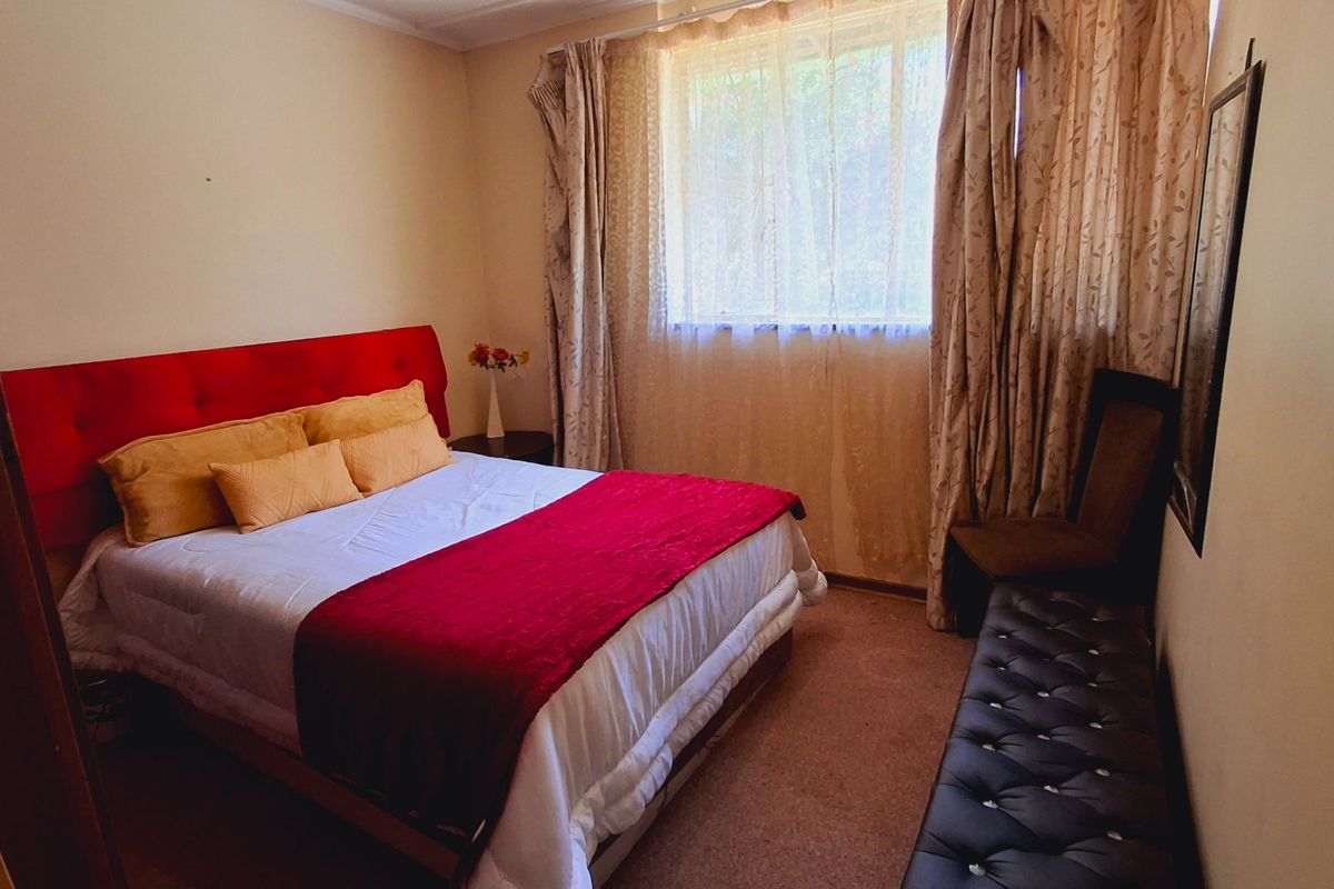 A cozy bedroom featuring carpeted flooring and a large window with curtains, providing natural light and a comfortable living space.