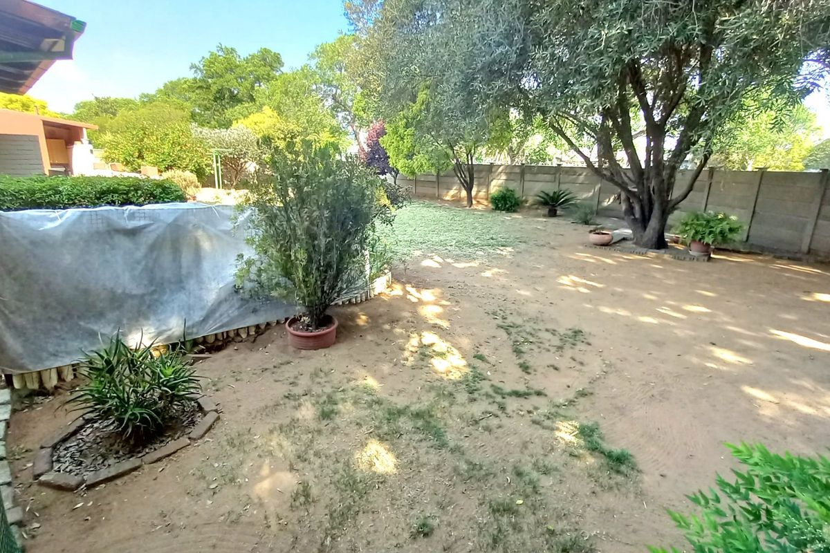 A spacious rear garden featuring mature trees and a precast concrete boundary wall, offering a blank canvas for landscaping improvements.