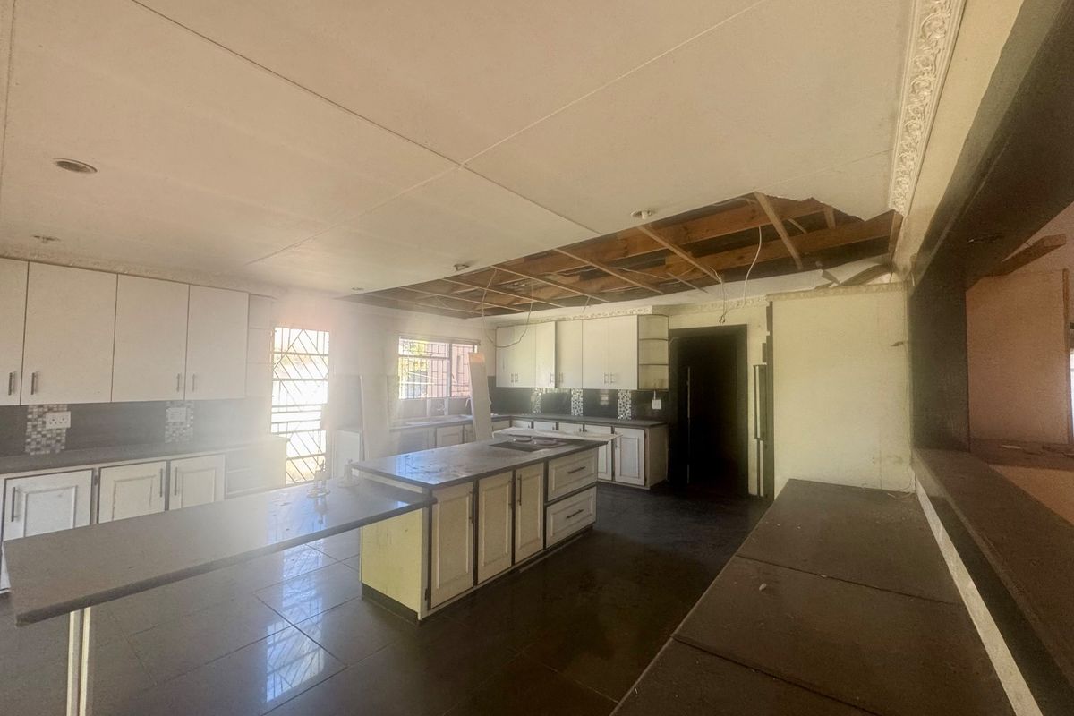 Spacious kitchen area featuring built-in cabinetry and a central island, currently requiring significant ceiling repairs and general refurbishment.