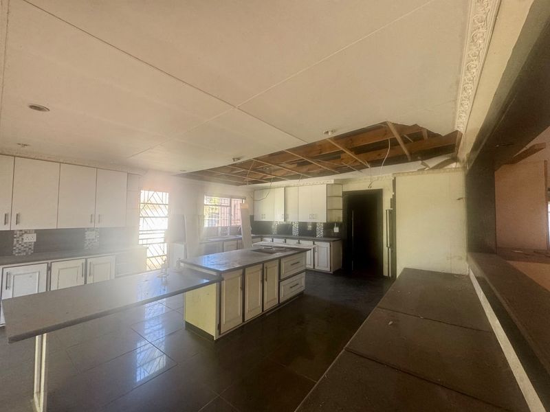 Spacious kitchen area featuring built-in cabinetry and a central island, currently requiring significant ceiling repairs and general refurbishment.