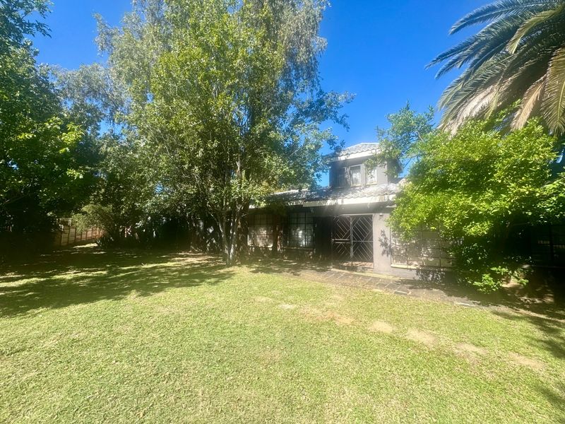 A view of the rear exterior of the property featuring a large, well-established garden with mature trees and a secure entrance.