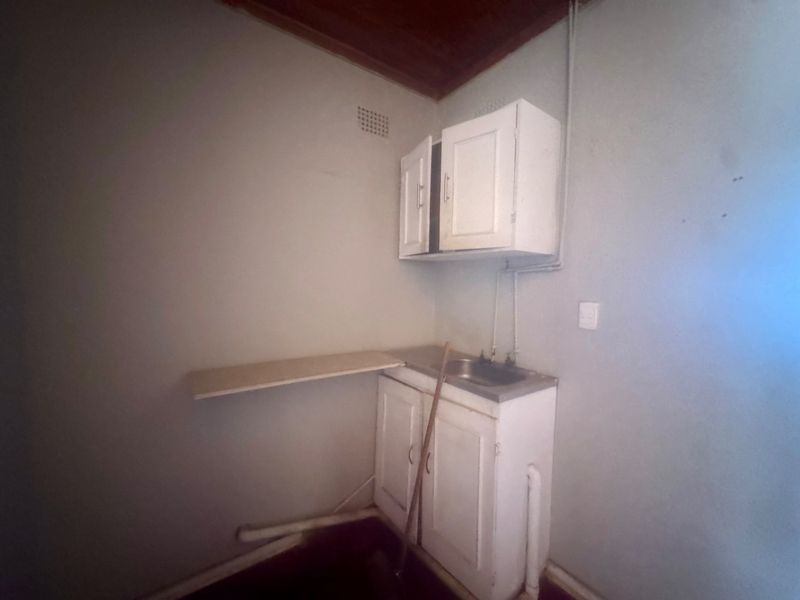 A basic utility or scullery area featuring built-in cabinetry, a stainless steel sink, and exposed plumbing, requiring cosmetic updates and maintenance.