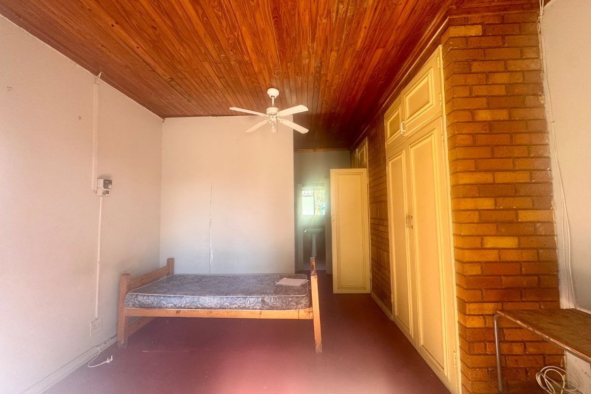 Bedroom featuring a timber ceiling, ceiling fan, built-in cupboards, and an exposed brick wall, offering a rustic aesthetic with potential for modernization.