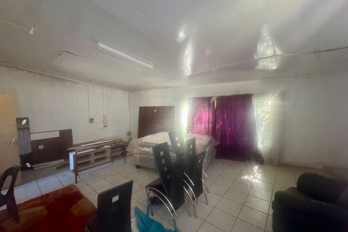 A spacious living area featuring tiled flooring and fluorescent lighting, currently in need of cosmetic updates and repairs to the walls and ceiling.
