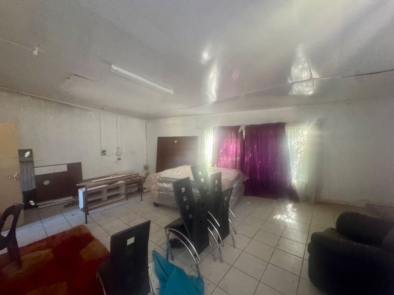 A spacious living area featuring tiled flooring and fluorescent lighting, currently in need of cosmetic updates and repairs to the walls and ceiling.