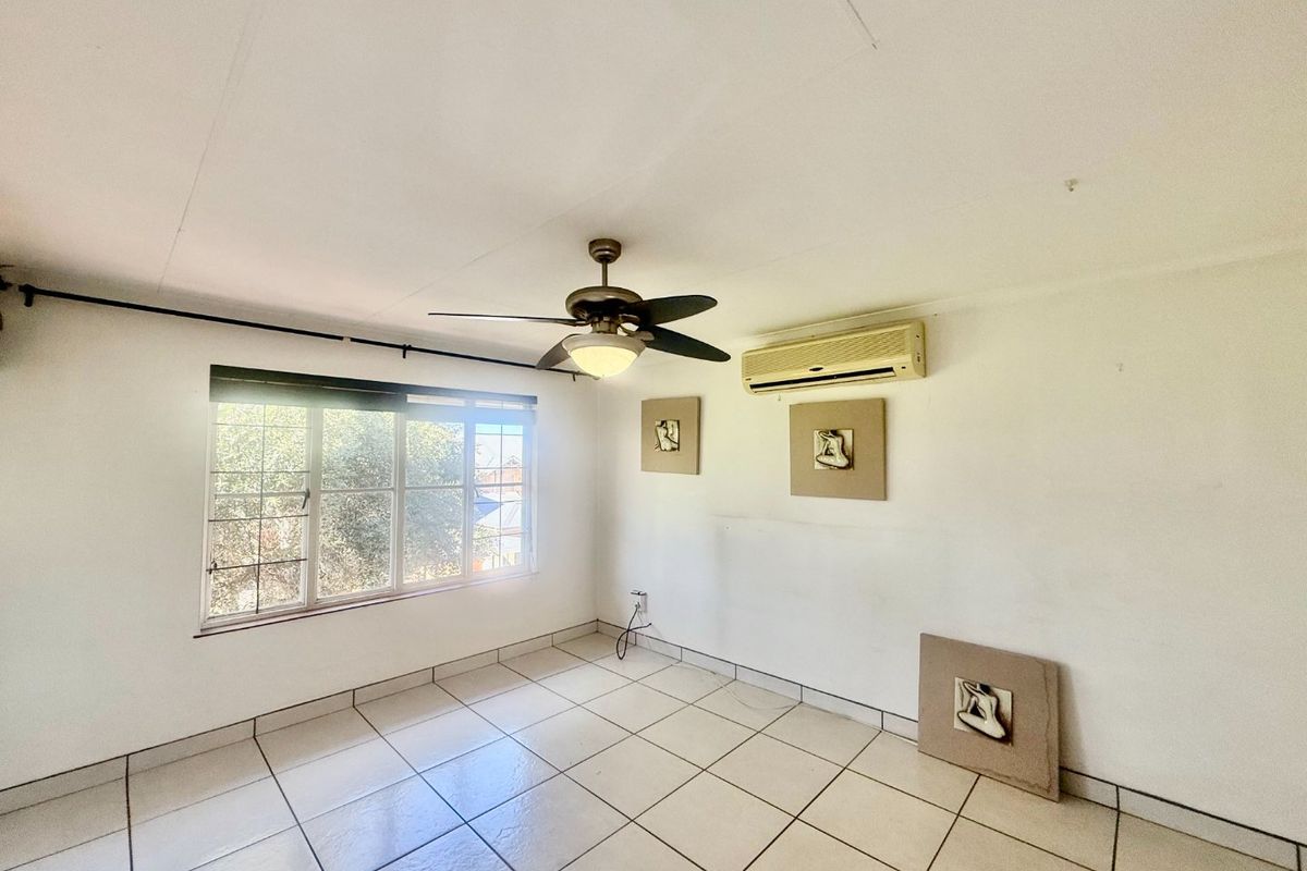 A bright, empty bedroom featuring tiled flooring, a ceiling fan, and a wall-mounted air conditioning unit.