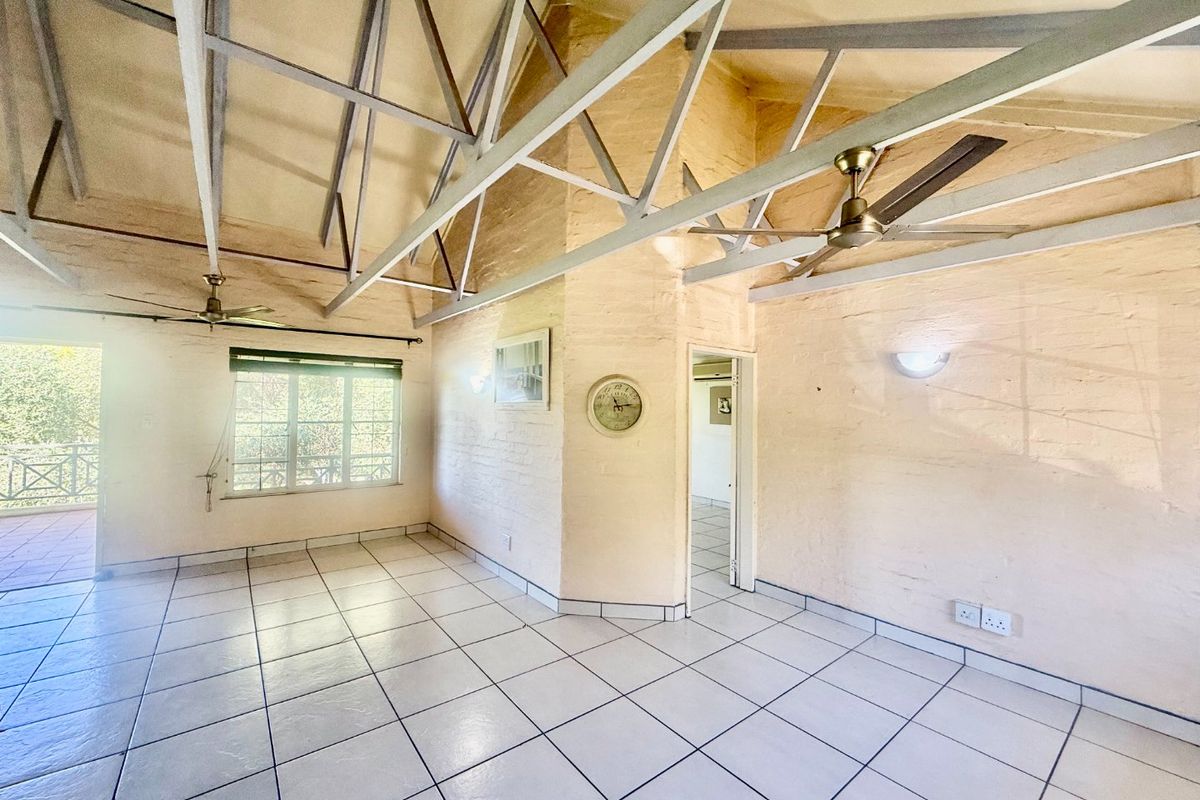 Spacious living area featuring high vaulted ceilings with exposed steel trusses, tiled flooring, and direct access to an outdoor balcony.