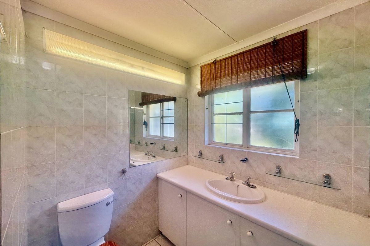 A functional bathroom featuring a vanity cabinet with integrated sink, wall-mounted mirror, toilet, and tiled finishes throughout.