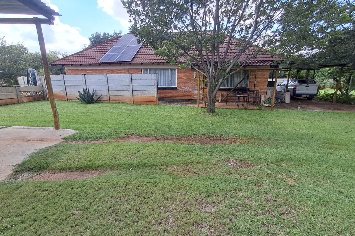 Rear view of a brick house featuring a tiled roof, solar panels, a covered patio area, and a spacious garden.