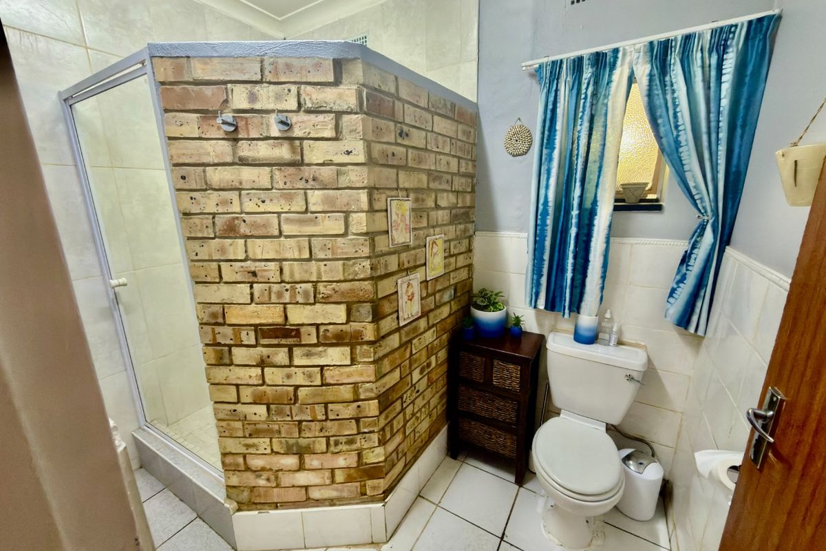 A bathroom featuring a brick-enclosed shower stall, tiled flooring, and a standard toilet suite with a small window.