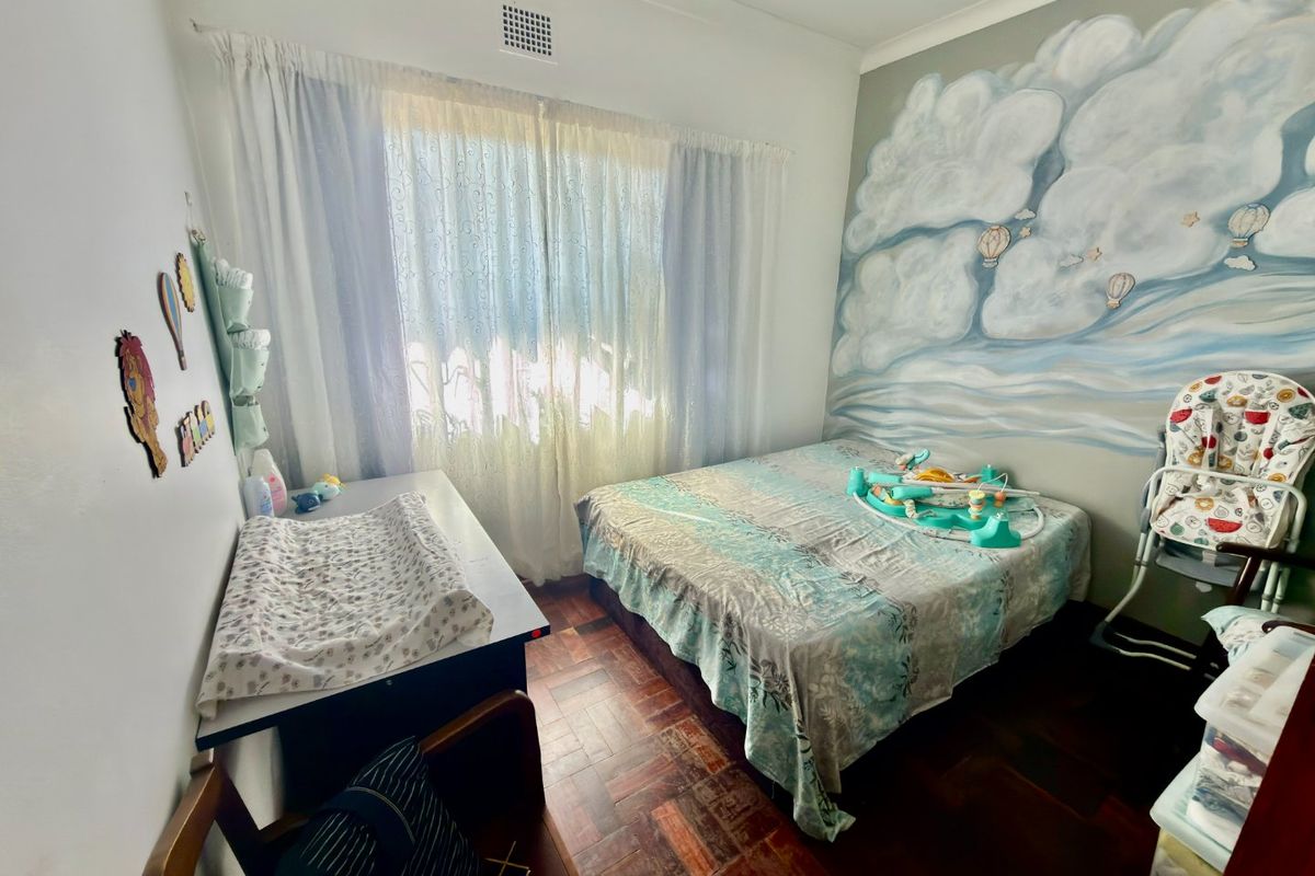 A bedroom featuring parquet flooring, a large window with curtains, and a decorative mural on the feature wall.