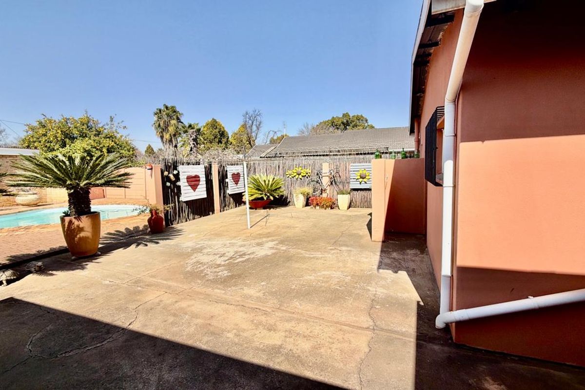 Rear exterior view featuring a concrete patio area adjacent to a swimming pool and boundary wall.