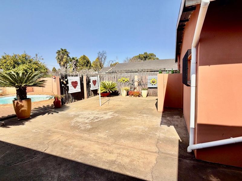 Rear exterior view featuring a concrete patio area adjacent to a swimming pool and boundary wall.