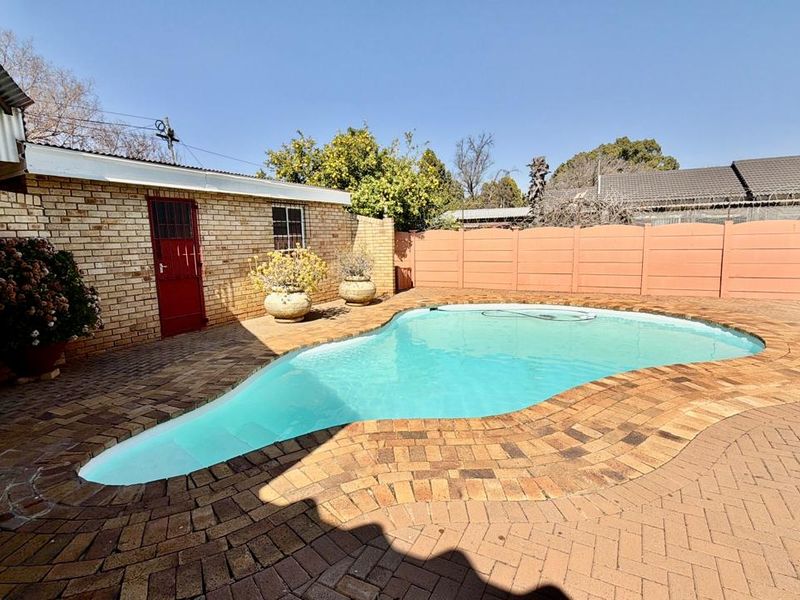 Outdoor pool area featuring a swimming pool surrounded by brick paving, enclosed by a combination of face brick and precast concrete boundary walls.