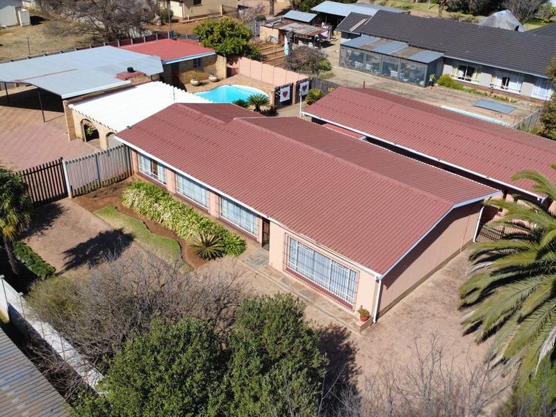 Aerial view of the property featuring a metal roof, swimming pool, paved driveway, and established garden areas within a fenced perimeter.