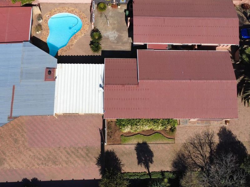 Aerial view of the property featuring a swimming pool, multiple roof sections, paved driveway, and established garden areas.