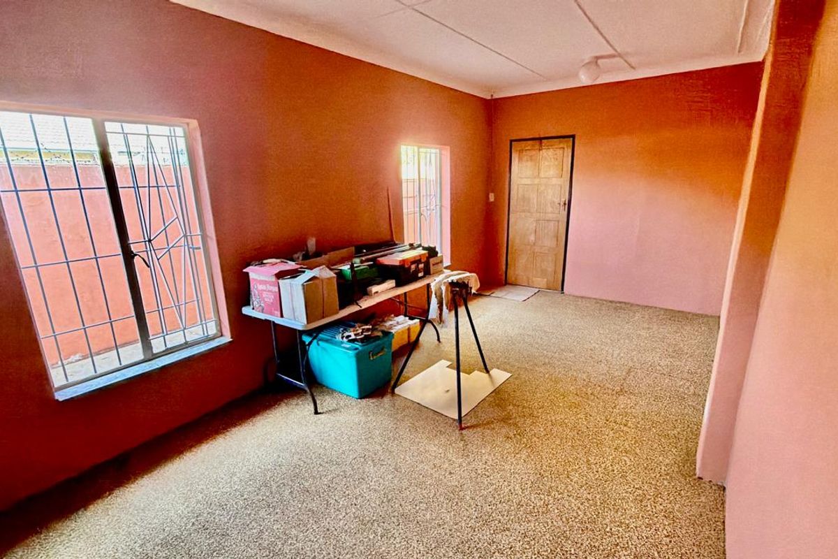 A vacant living area featuring carpeted flooring, security bars on windows, and a timber entrance door.