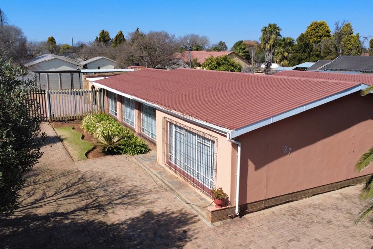 Aerial view of a single-story residential property featuring a corrugated metal roof, paved driveway, and secure window bars.
