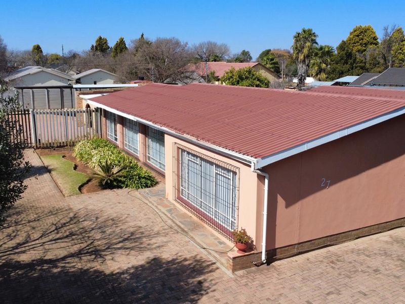 Aerial view of a single-story residential property featuring a corrugated metal roof, paved driveway, and secure window bars.