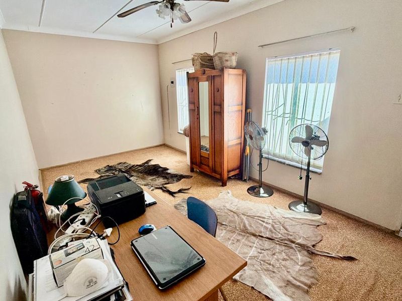 A bedroom featuring carpet flooring, a ceiling fan, and vertical blinds, currently utilized as a home office space.