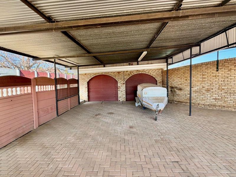 A spacious covered carport or garage area featuring brick paving, brick walls, and dual roller shutter doors, providing secure off-street parking.