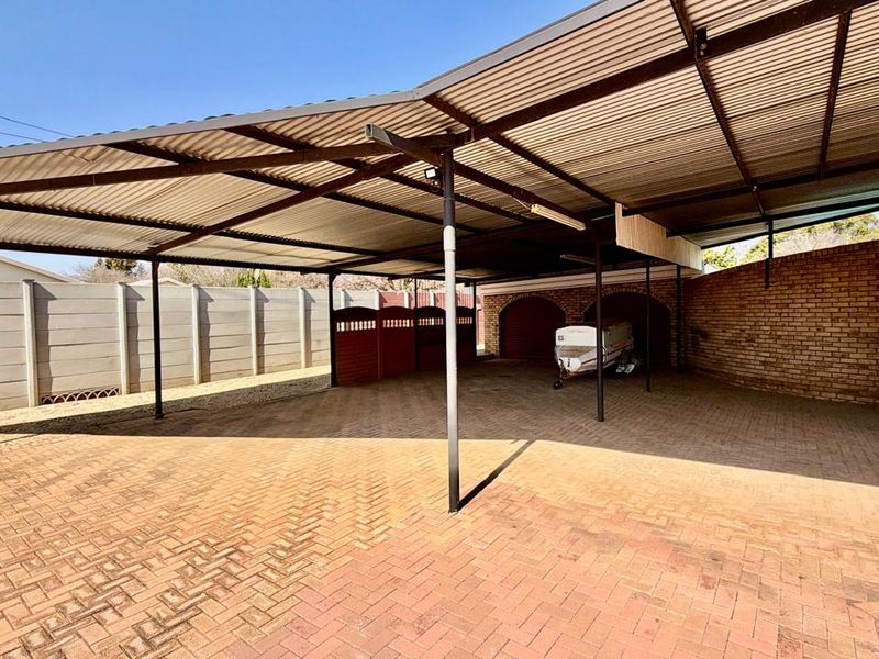 A spacious, covered carport area featuring paved flooring, brick archways, and sturdy steel support structures, providing ample sheltered parking space.