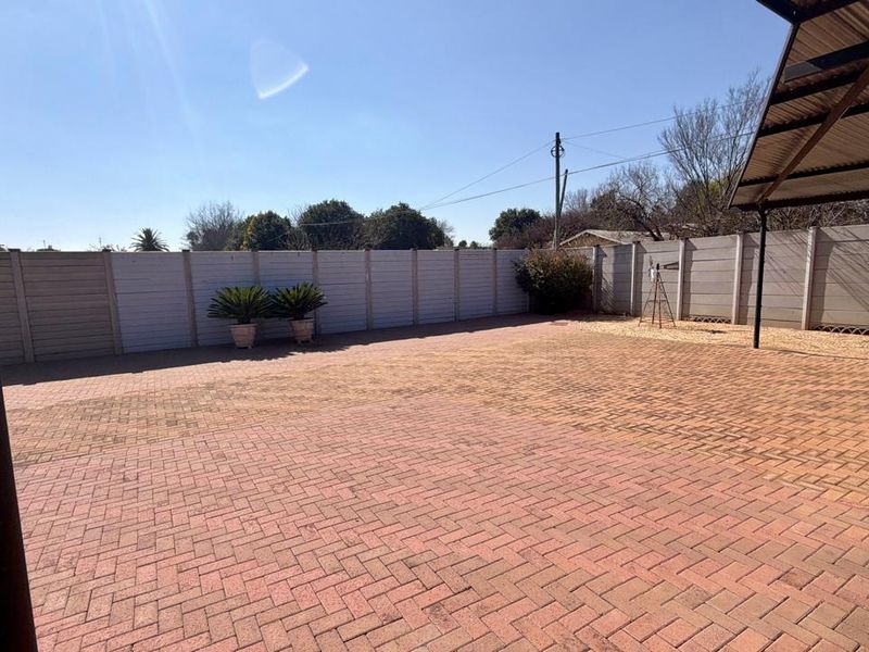 A spacious, paved outdoor patio area featuring a covered section and enclosed by a precast concrete boundary wall.