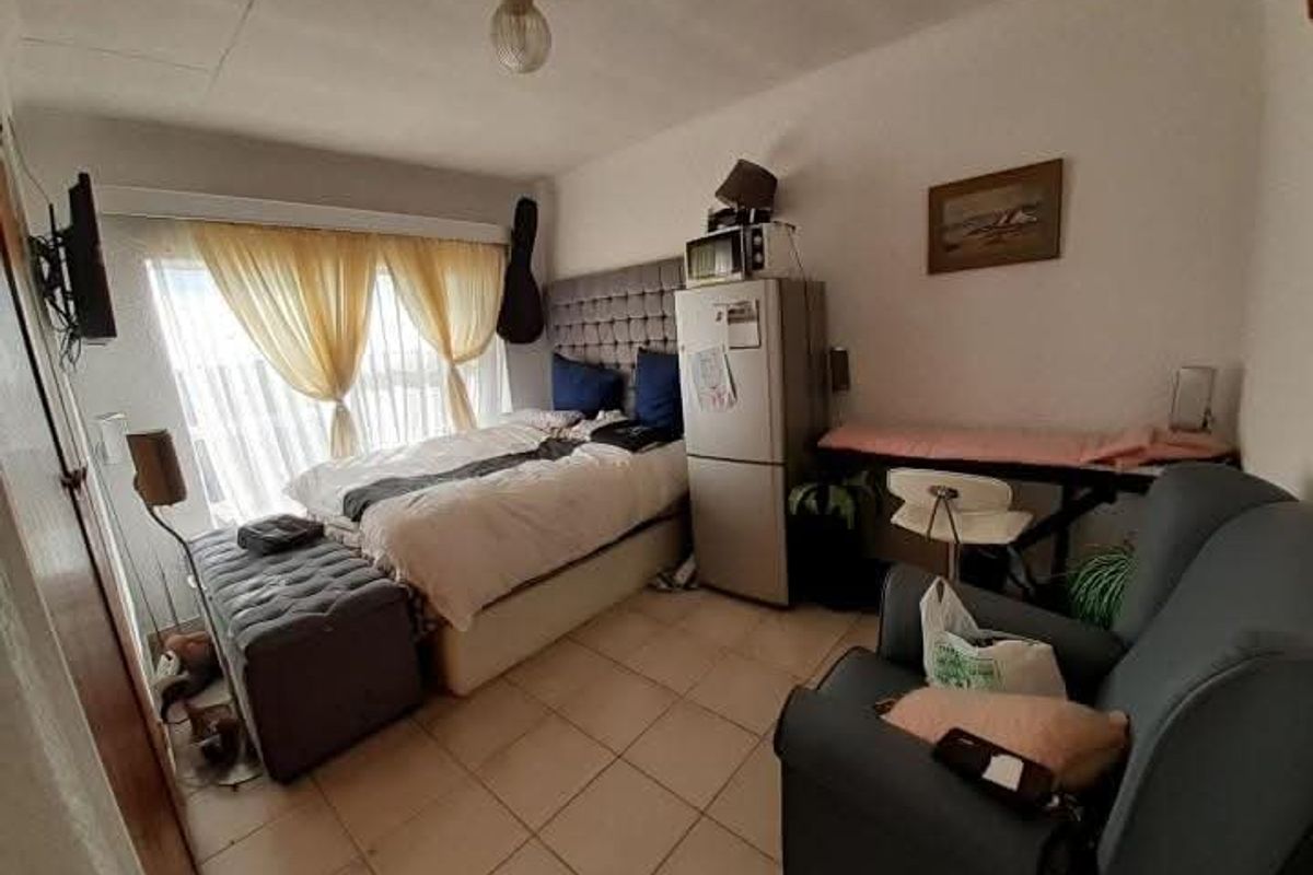 A compact bedroom featuring tiled flooring and a built-in headboard, with large windows allowing for natural light.