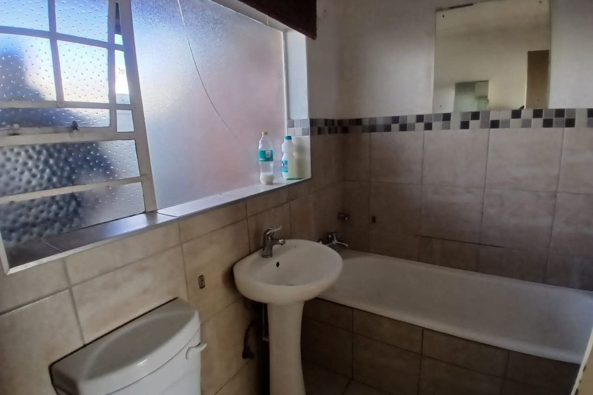 A functional bathroom featuring a pedestal basin, bathtub, and toilet with tiled finishes, requiring some maintenance and cosmetic updates.