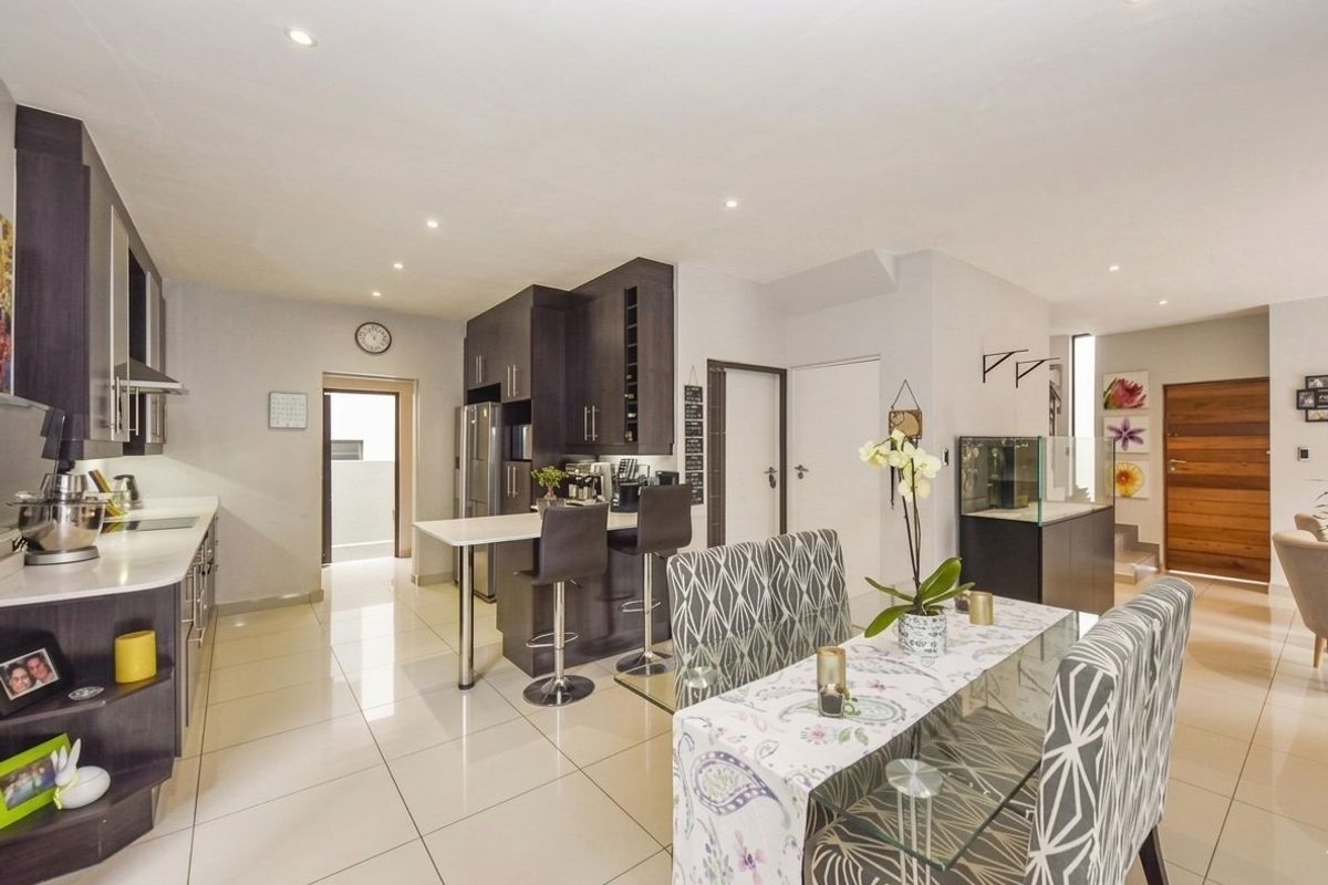 Modern open-plan kitchen and dining area featuring dark cabinetry, stone countertops, breakfast bar, and polished tiled flooring with recessed lighting.