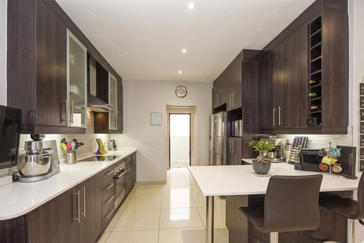 Modern galley-style kitchen featuring dark wood cabinetry, stone countertops, integrated appliances, and sleek tiled flooring with recessed lighting.