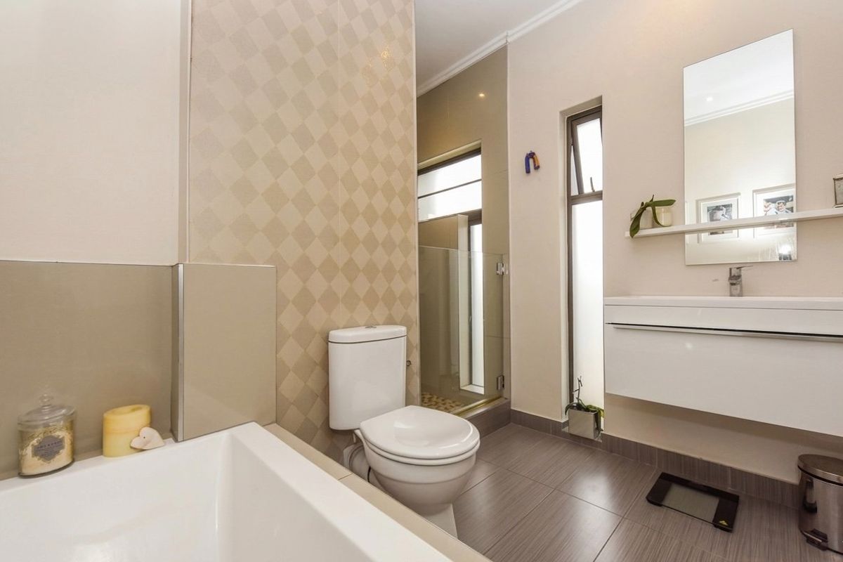 Modern bathroom featuring a built-in bathtub, wall-mounted vanity, glass shower enclosure, and neutral tiled finishes.