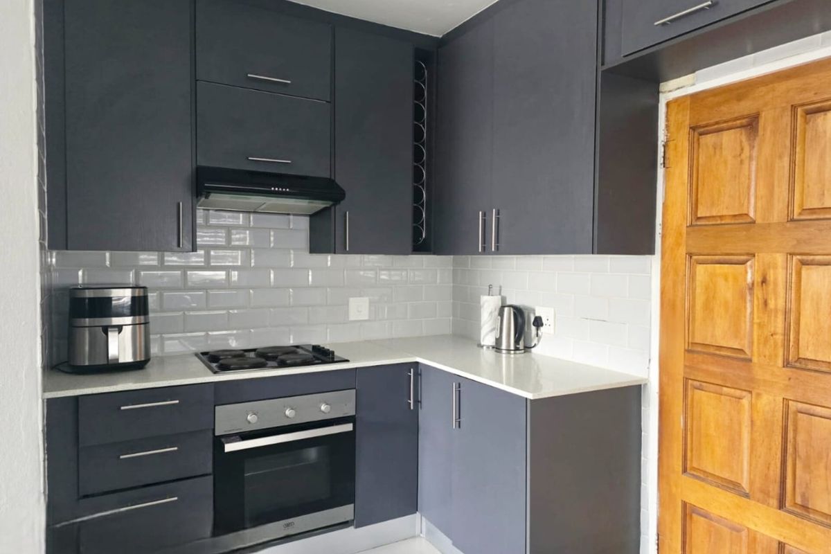 Modern kitchen featuring dark grey cabinetry, white subway tile backsplash, stone countertops, and integrated stainless steel appliances.