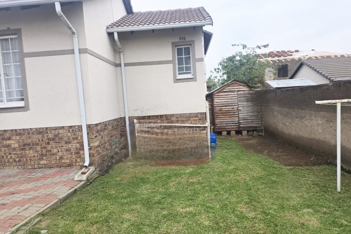 Rear exterior view of the house featuring a paved patio area, lawn, boundary wall, and a detached wooden storage shed.