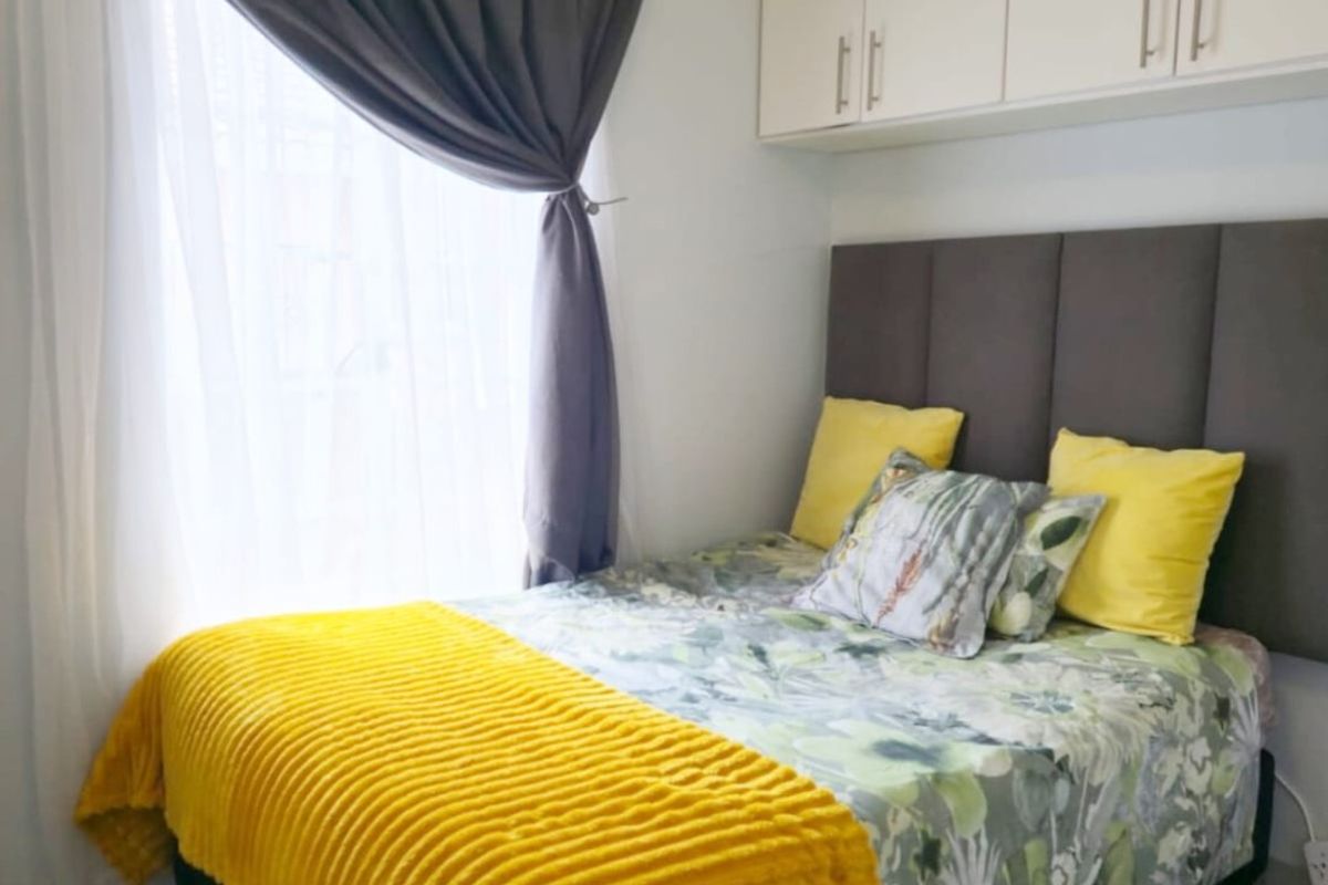 A compact bedroom featuring tiled flooring, coved ceilings, and practical built-in overhead storage cabinetry.
