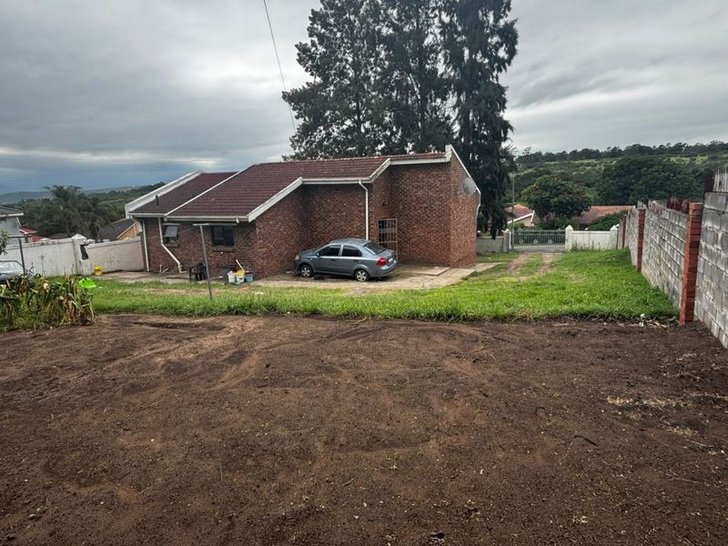 Rear view of a brick house featuring a tiled roof, concrete driveway, and a large unlandscaped yard area enclosed by boundary walls.