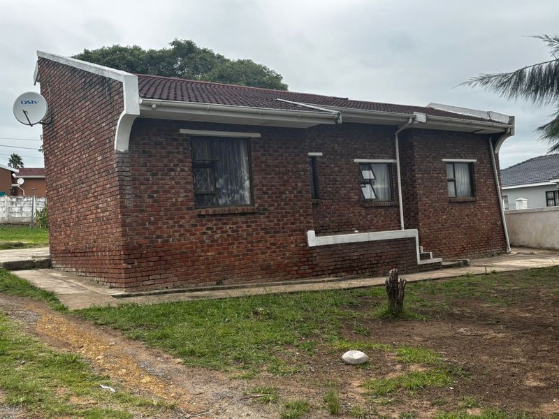 Rear view of a single-story face brick house featuring a tiled roof, concrete apron, and steel-framed windows set on a grassed plot.