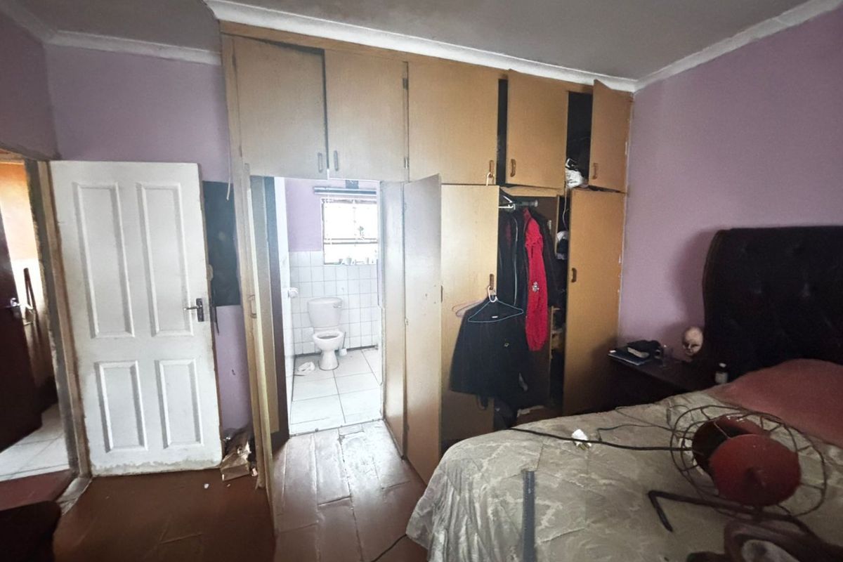 Bedroom featuring built-in cupboards and an attached en-suite bathroom. The room requires cosmetic updates and flooring repairs to improve its overall condition.