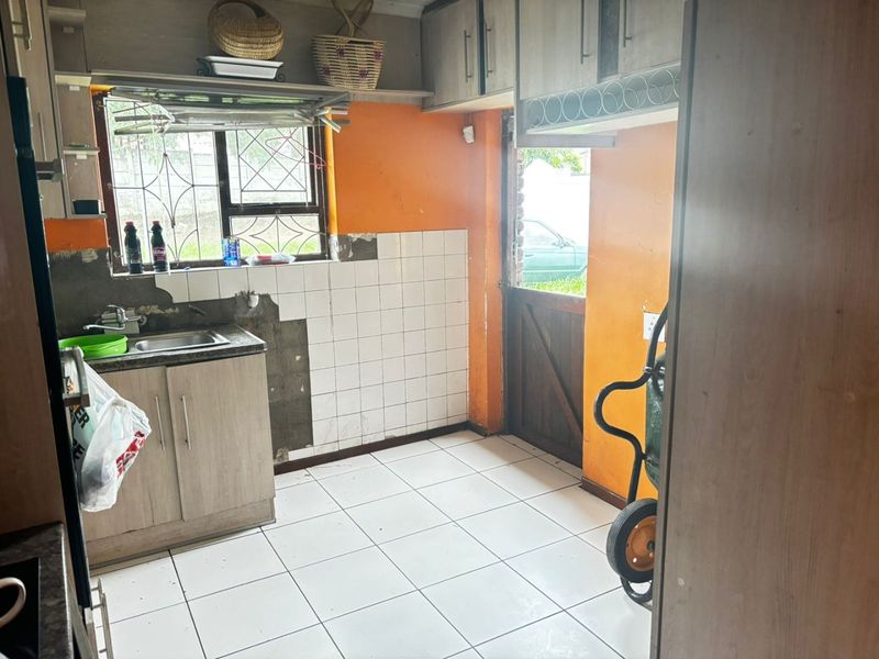 A functional scullery area featuring built-in cabinetry, a stainless steel sink, and tiled flooring, currently requiring cosmetic updates and wall repairs.