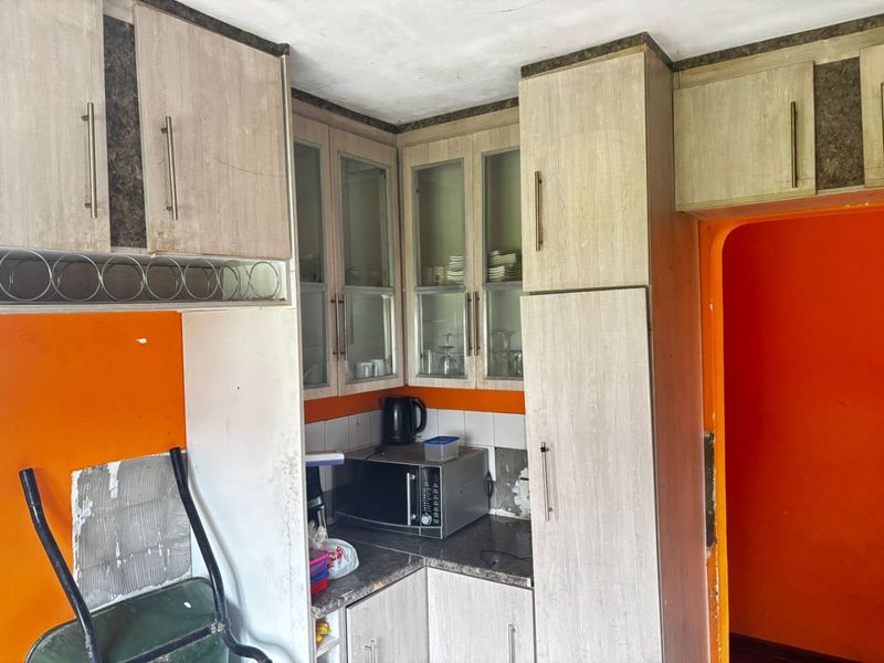A dated kitchen area featuring wood-look cabinetry, glass-fronted display cupboards, and a tiled backsplash, currently requiring cosmetic updates and wall repairs.