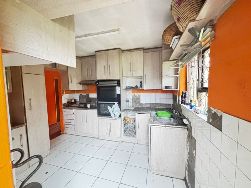 A dated kitchen featuring built-in cabinetry, a double oven, and tiled surfaces. The space requires renovation to address damaged wall finishes and worn cabinetry.