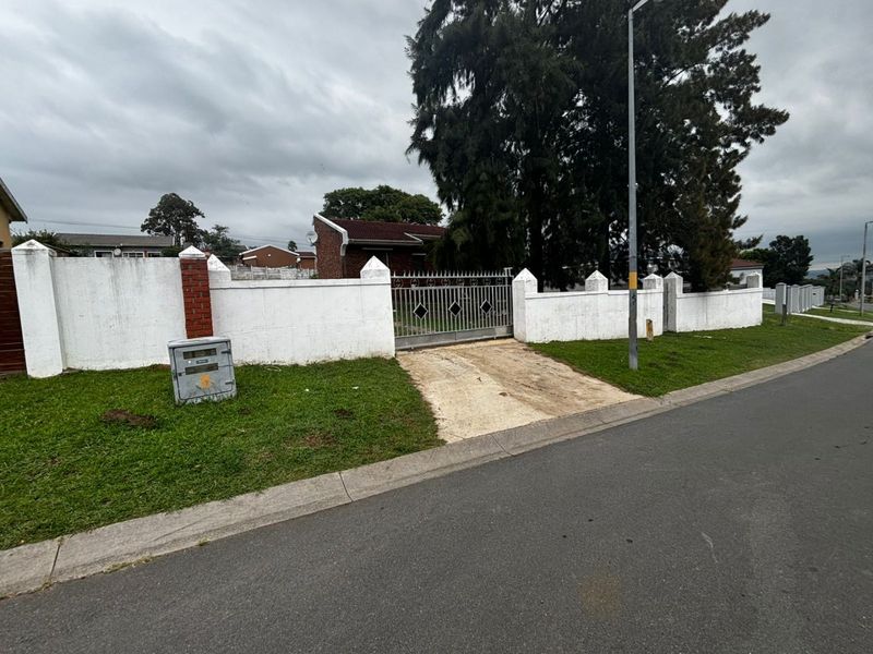 Front view of the property featuring a gated entrance, perimeter wall, and concrete driveway access from the street.