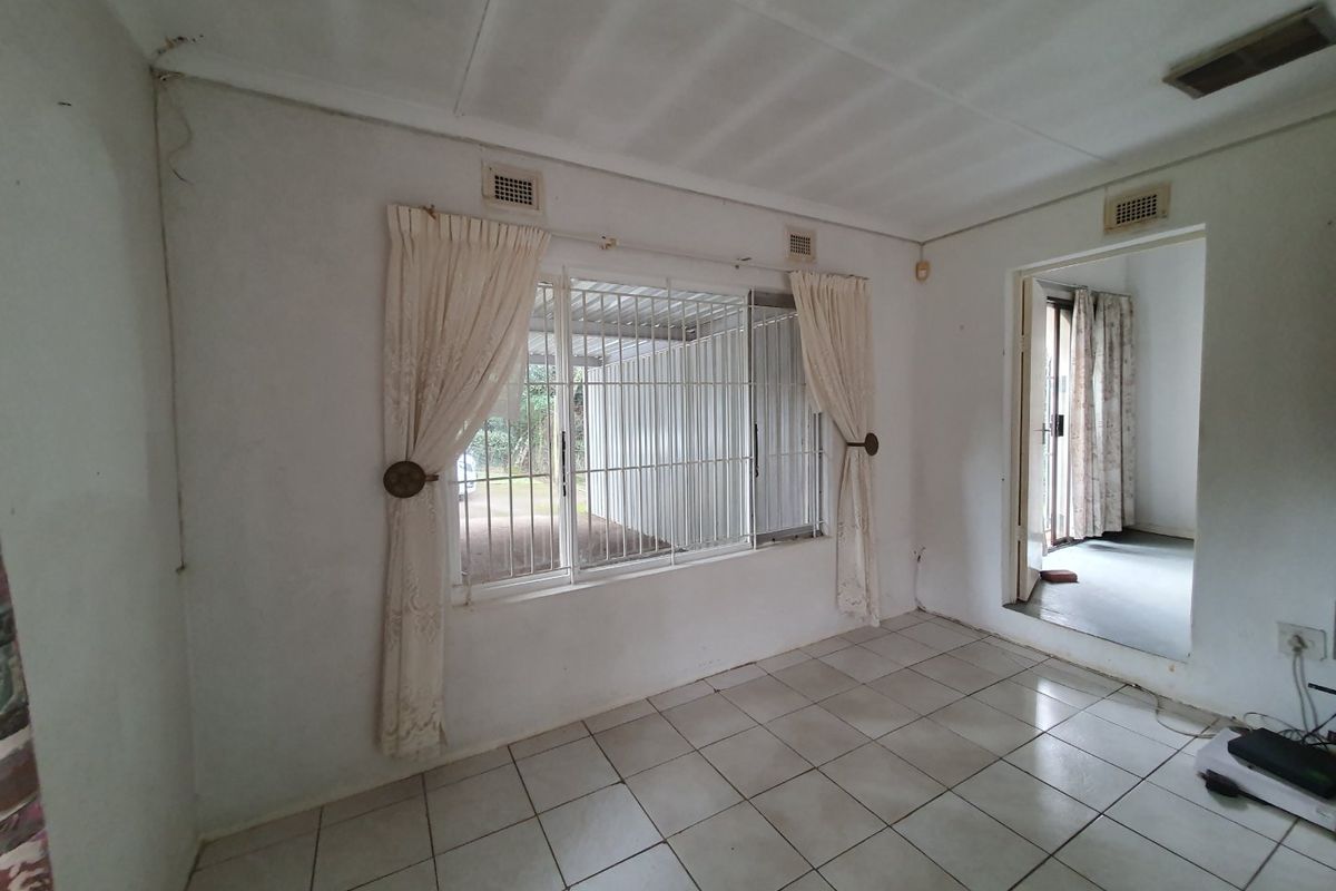 A vacant living area featuring tiled flooring, security bars on windows, and direct access to an adjacent room.
