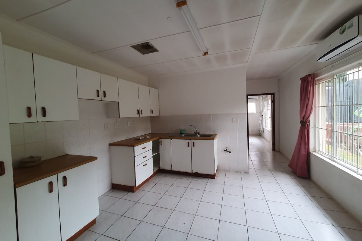 A functional kitchen featuring white cabinetry, tiled flooring, and a stainless steel sink, offering a blank canvas for potential renovation and modernization.