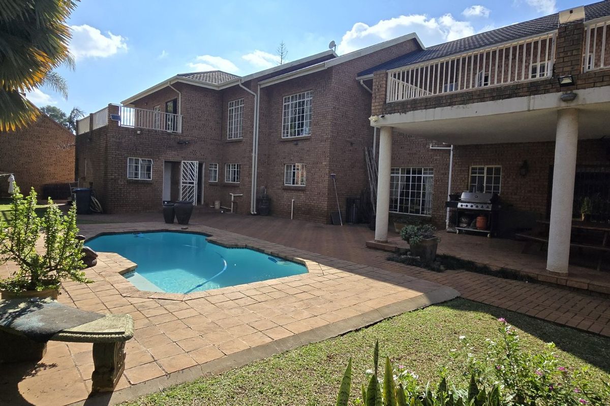 Rear view of a multi-story brick house featuring a swimming pool, paved patio area, and an upper-level balcony overlooking the garden.