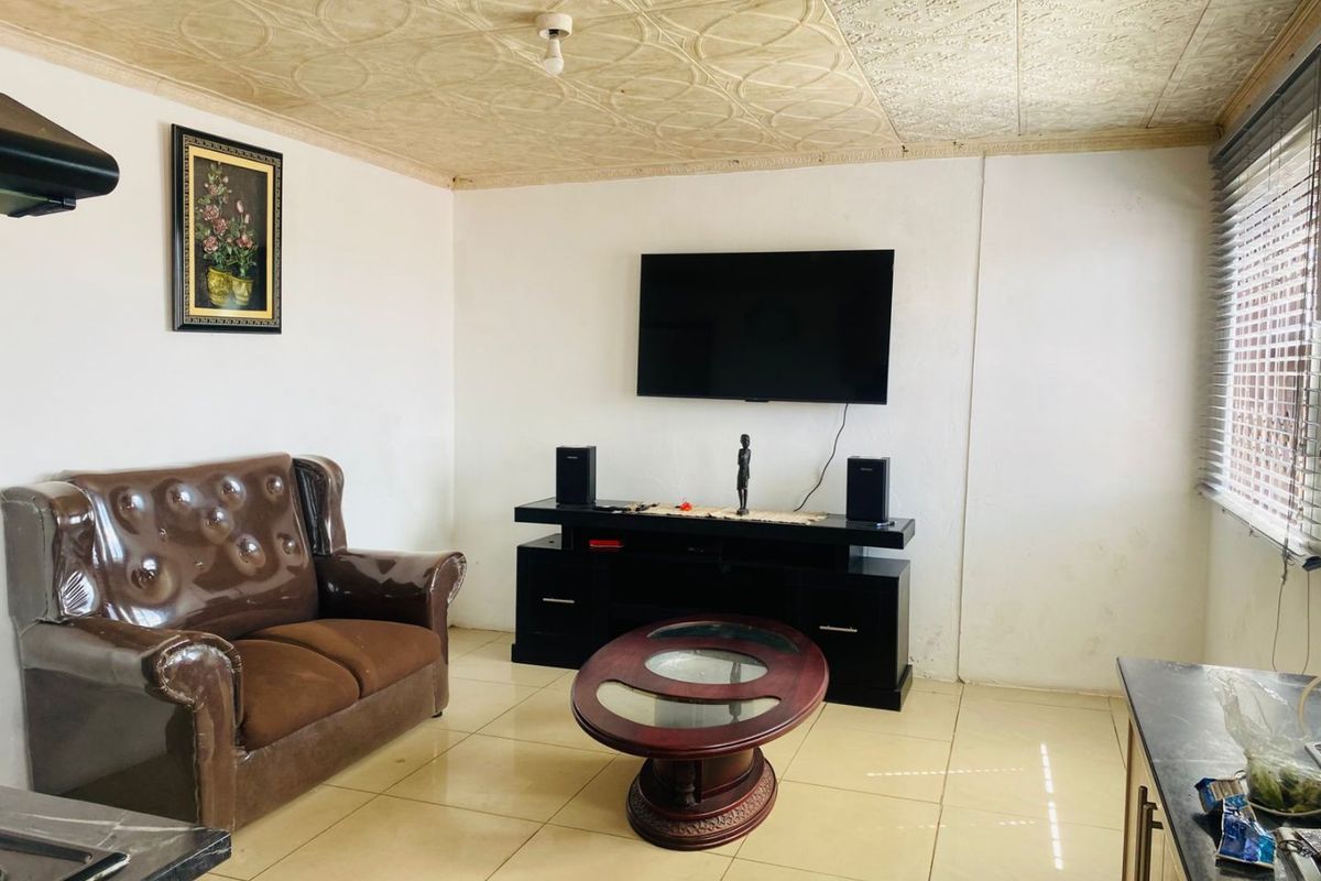 A living room featuring tiled flooring, a textured ceiling, and venetian blinds, offering a functional space with potential for cosmetic updates.