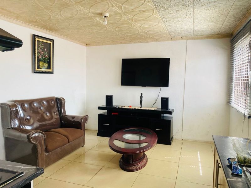 A living room featuring tiled flooring, a textured ceiling, and venetian blinds, offering a functional space with potential for cosmetic updates.