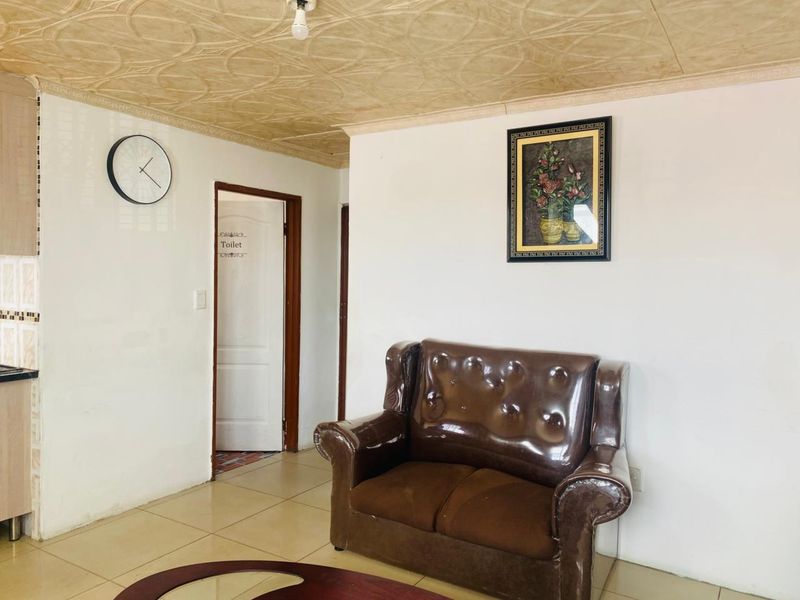 A living area featuring tiled flooring and a textured ceiling, providing a functional space with access to an adjacent toilet.