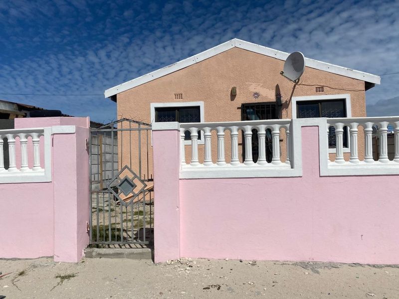 Front elevation of a single-story house featuring a pink boundary wall with balustrades, a metal gate, and security bars on the windows.